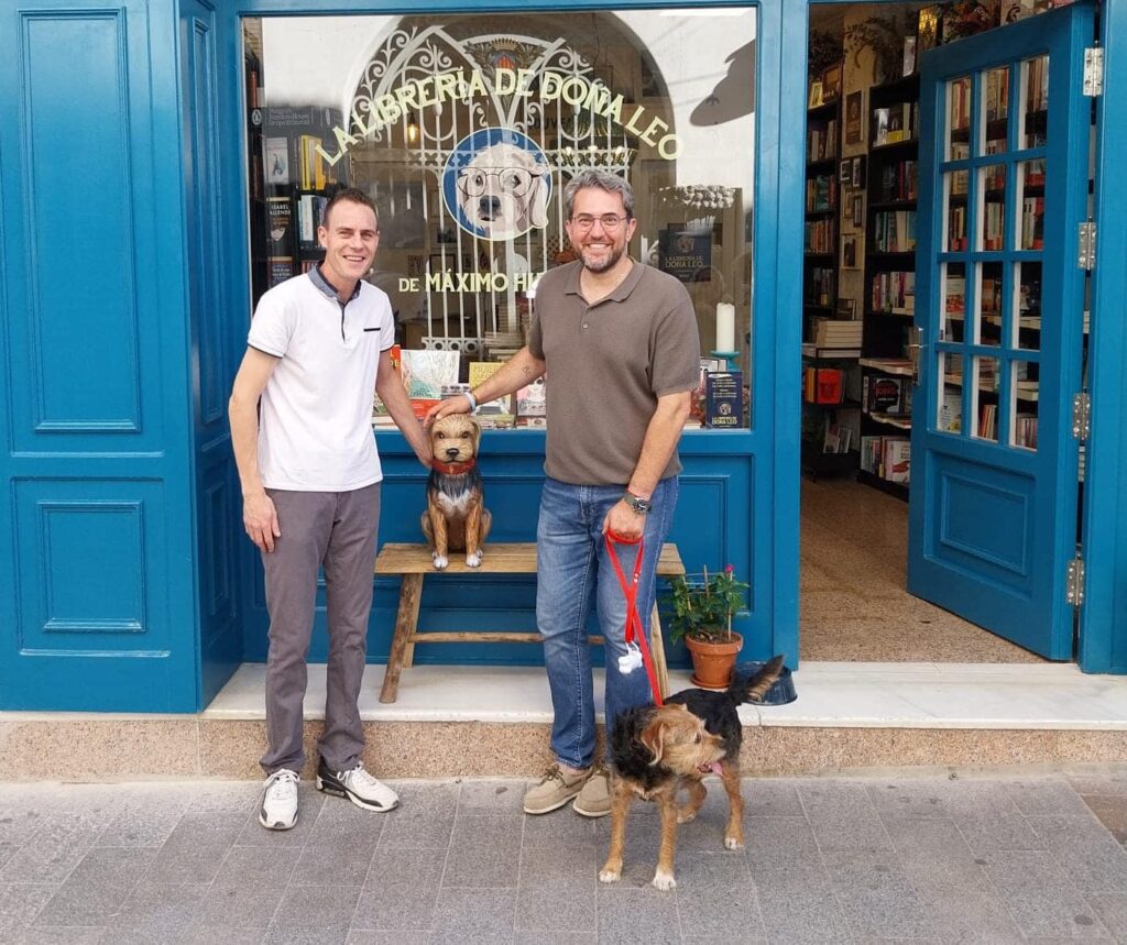 Son Emilio Tamarit Simón y Màxim Huerta posando, y tienen al medio una mesa de madera en la que han puesto encima, un ninot de falla de un perro, que representa a la perrita de Màxim Huerta. Y en la foto, además Màxim Huerta agarra la correa en la que va atada su perrita de verdad. La perra es de color marrón y negro.