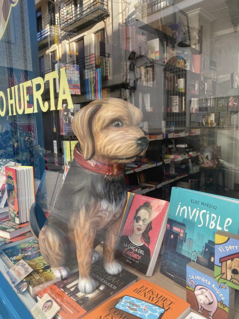 Ninot de falla. Es un ninot de falla de un perro, que está expuesto en la vitrina de una librería. El ninot de falla está encima de algunos de los libros.